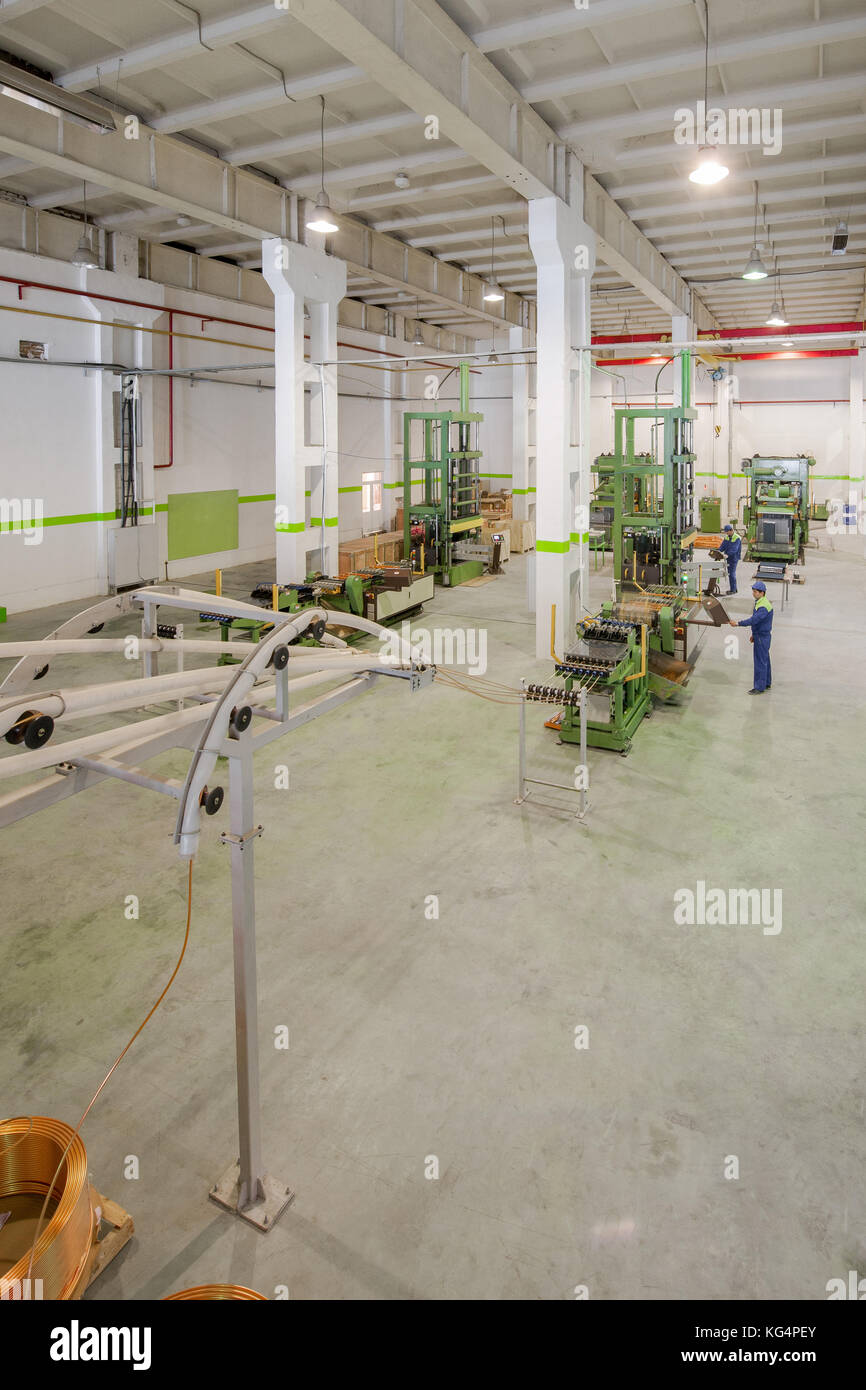 at the factory equipment for the deployment of copper tubes from rolls and cutting governed by workers Stock Photo