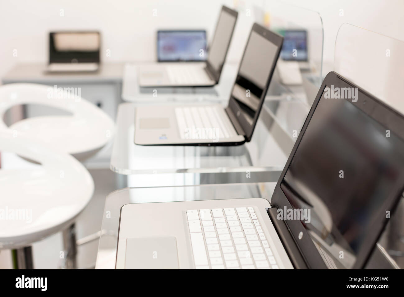 New, open laptops, on a glass desktop; modern white chairs in