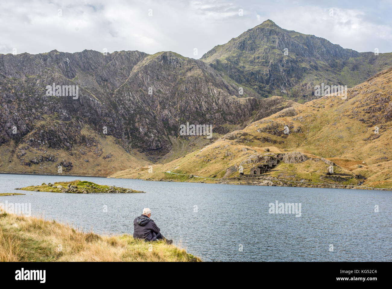 Solitary white-haired man sits gazes at the peak of mount Snowdon, the highest mountain in England and Wales. Stock Photo
