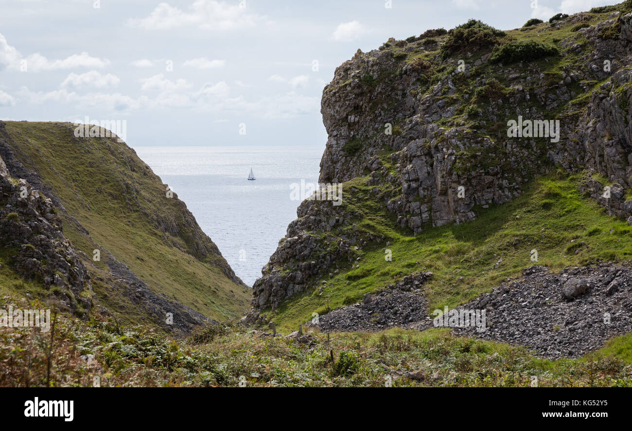 A yacht sailing along the coast of the Gower peninsula at the valley above Paviland Cave near Port Eynon Stock Photo
