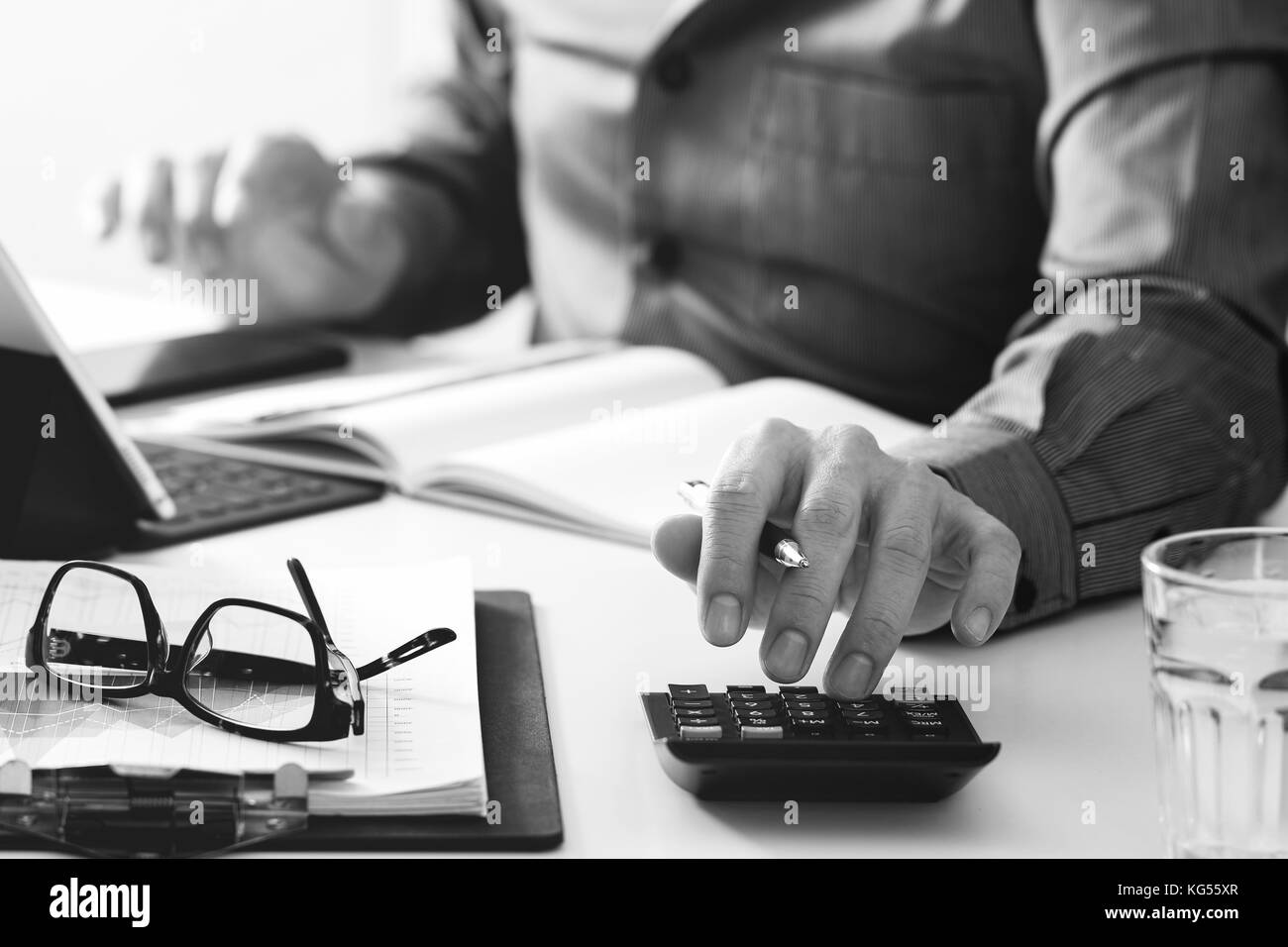 businessman hand working with finances about cost and calculator and latop with mobile phone on withe desk in modern office,black and white Stock Photo