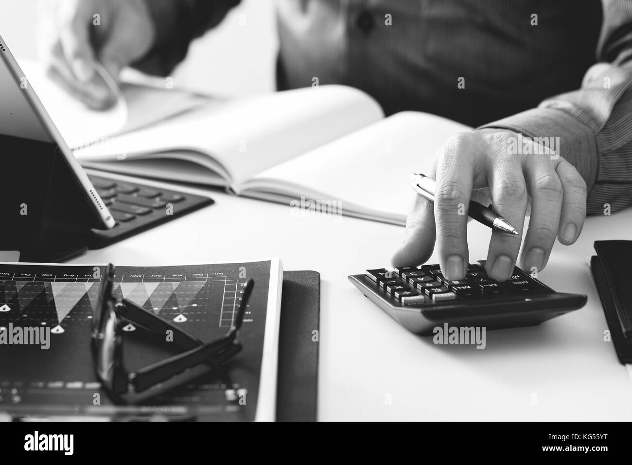 businessman hand working with finances about cost and calculator and latop with mobile phone on withe desk in modern office,black and white Stock Photo