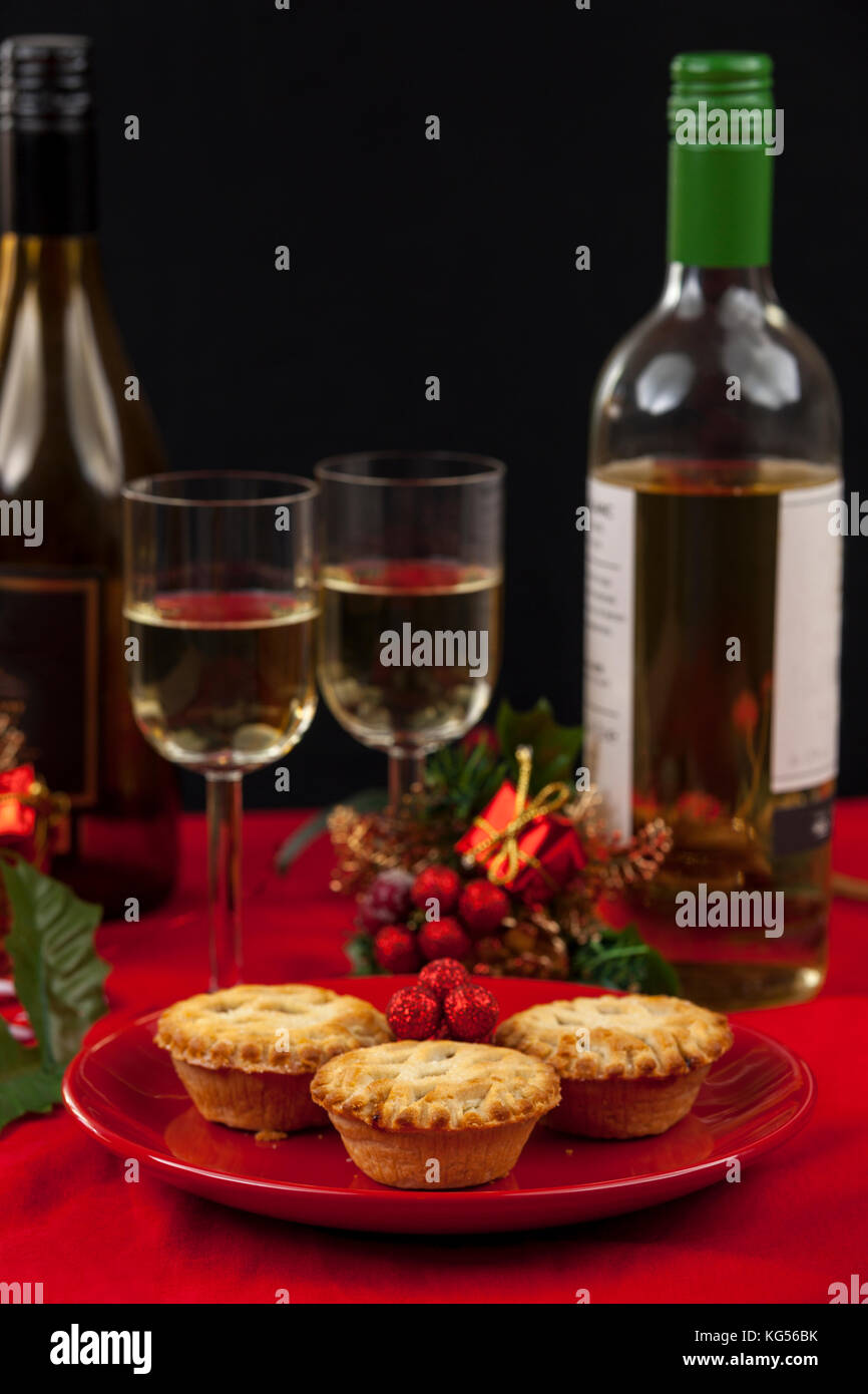 Mince pies on a red plate with glasses and bottles of white wine on a