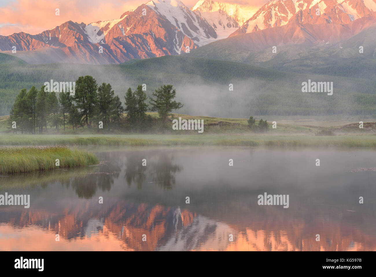 Beautiful pink sunrise over a lake, mountains covered with snow, fog ...