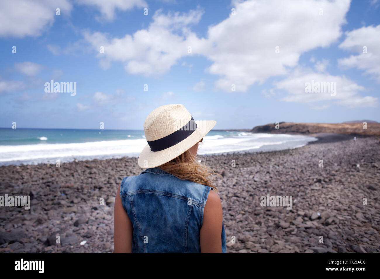 woman back with hat. looking over the sea. standing on a stones beach ...
