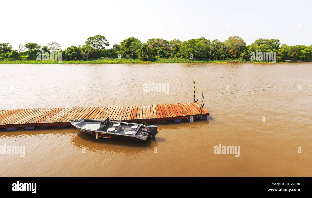 Wooden dock with a boat anchored on it. Dock in the middle of the river. Tourism or fishing background on nature. Stock Photo
