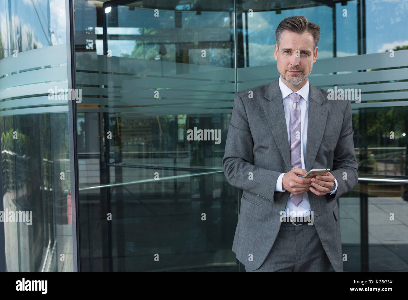 businessman with Smartphone in front of glass revolving door Stock Photo