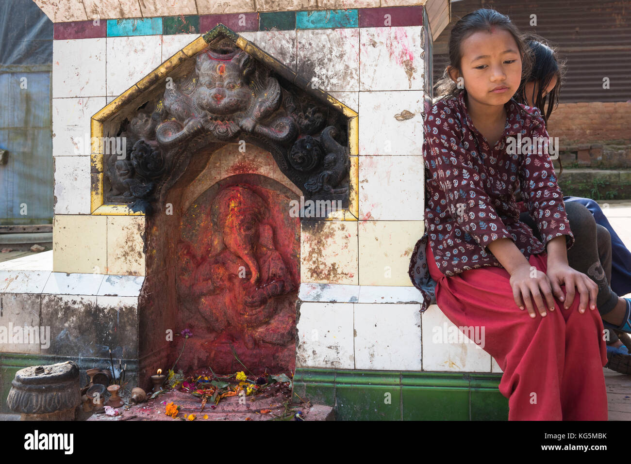 Bhaktapur, Kathmandu, Bagmati area, Nepal Little girl sitting beside the statue of Ganesh Stock Photo