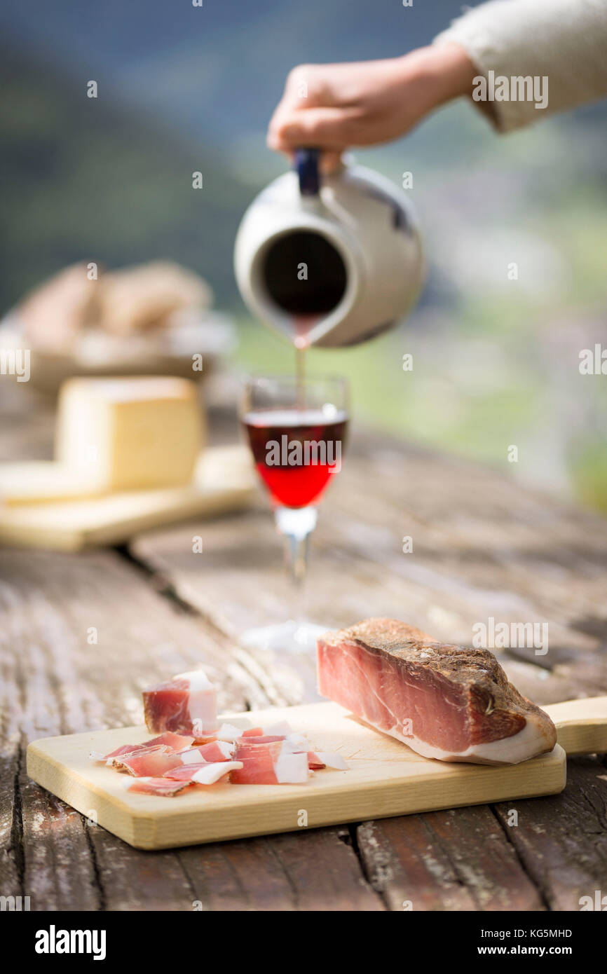 a piece of bacon (speck) with a hand filling a glass of wine, Bolzano province, South Tyrol, Trentino Alto Adige, Italy, Stock Photo