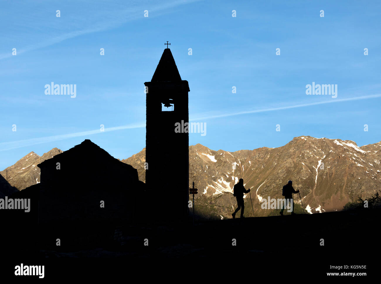 Silhouettes of hikers at the old church at dawn, San Romerio Alp, Brusio, Canton of Graubünden, Poschiavo valley, Switzerland Stock Photo