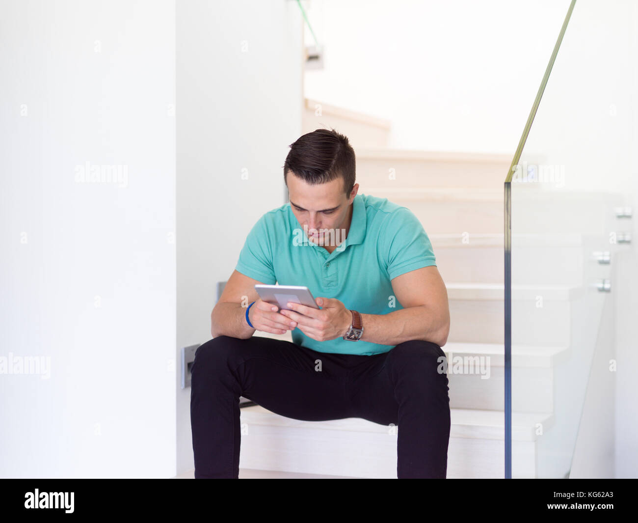 Handsome casual young man using a tablet while sitting on the stairs at ...
