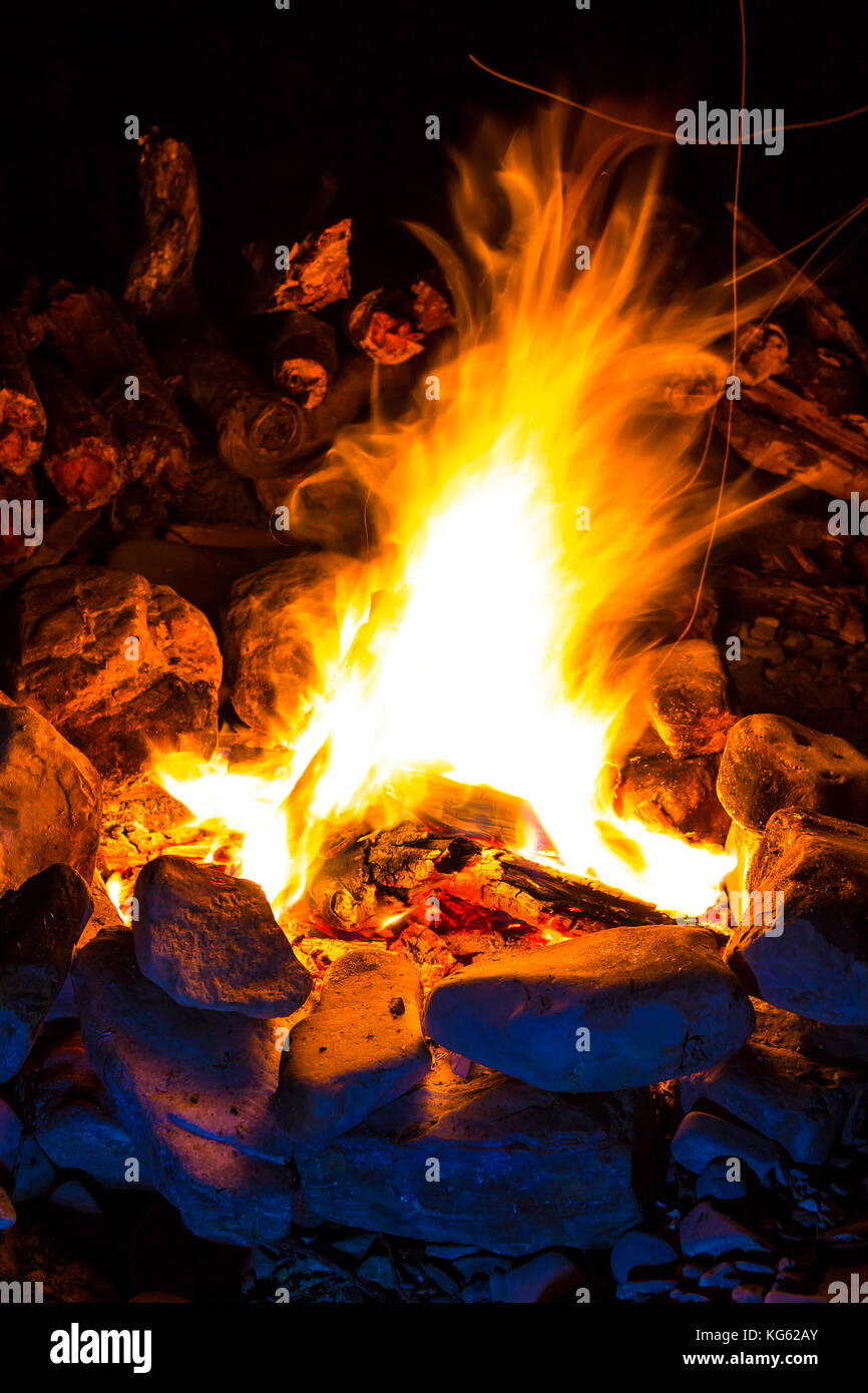 Campfire surrounded by rocks and a pile of firewood behind it at night ...