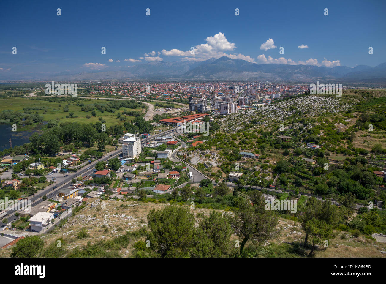 The city of Shkoder, Albania taken from the Rozafa Castle.  A wide main road leads the eye into the town surrounded by grass and trees. Stock Photo
