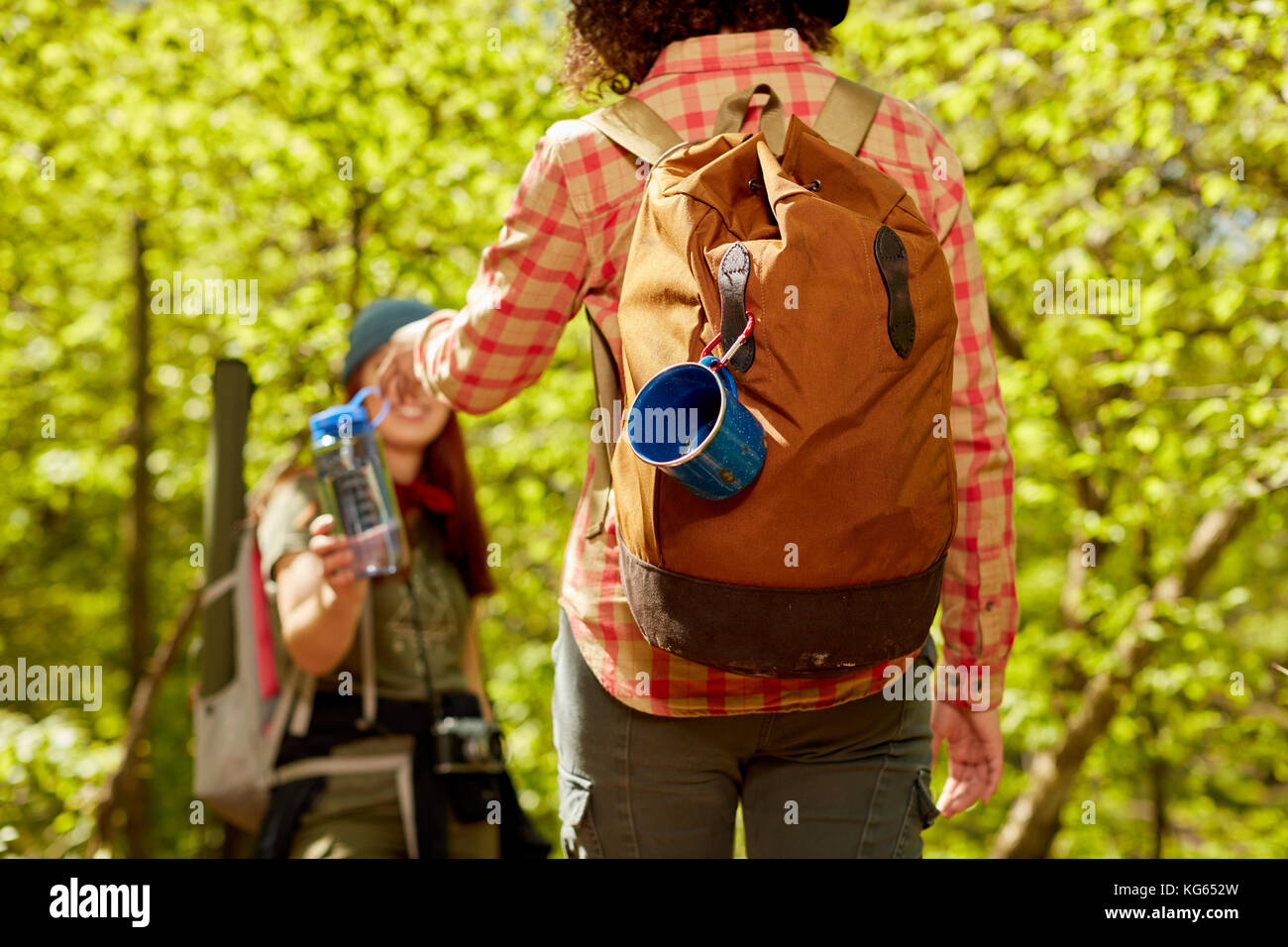 Two female friends hiking in woodland stopping for a break to take a drink from a flask in a close up rear view Stock Photo