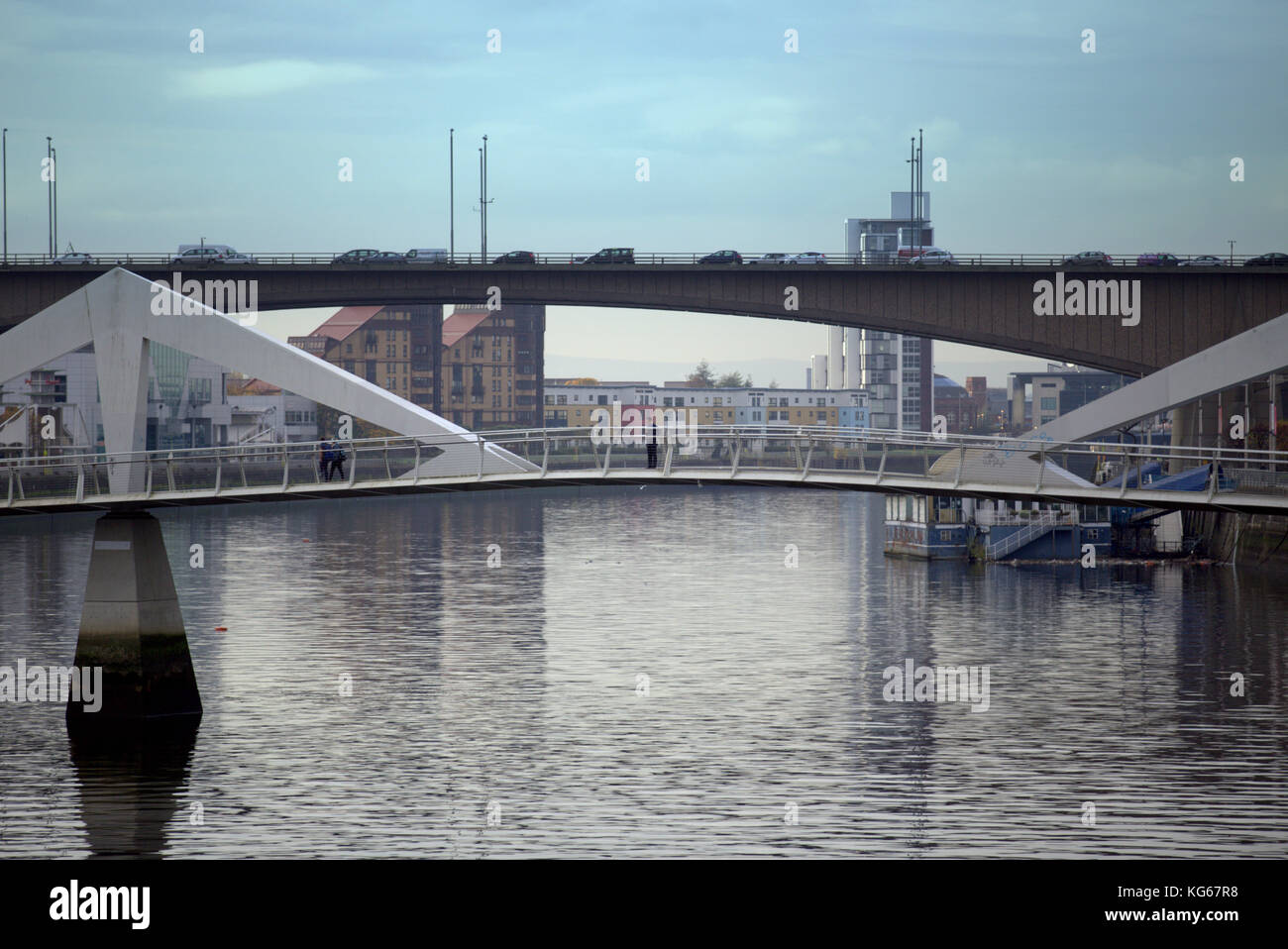 man on The Tradeston Bridge known as the squiggly bridge)[1] is a pedestrian bridge across the River Clyde in Glasgow with the kingston bridge behind. Stock Photo