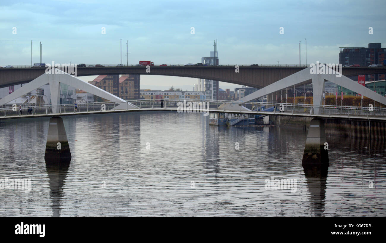 man onThe Tradeston Bridge known as the squiggly bridge)[1] is a pedestrian bridge across the River Clyde in Glasgow with the kingston bridge behind. Stock Photo