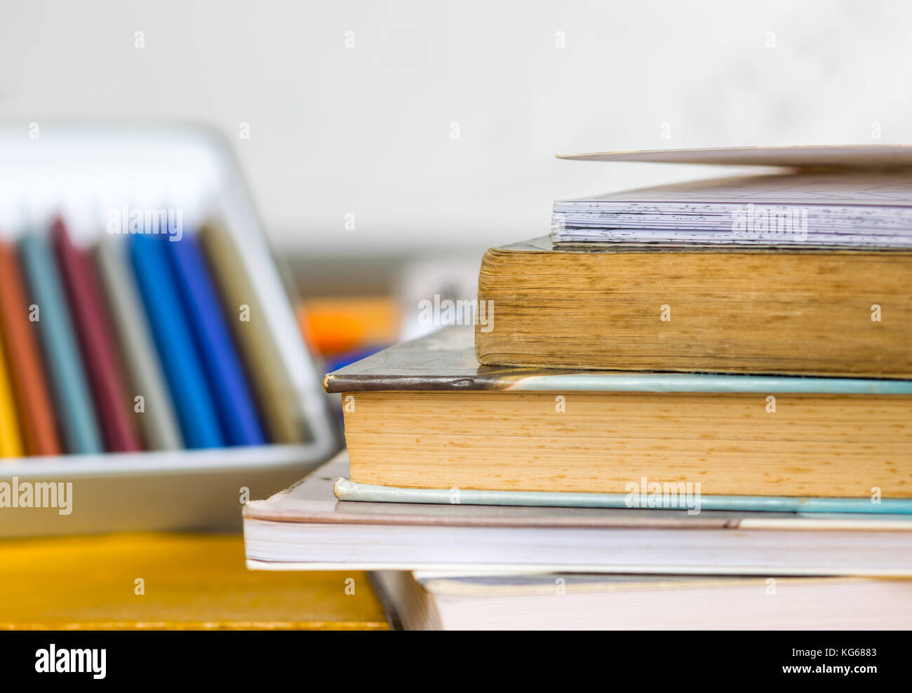 Coloring pencils, pens and closed books and notebooks on top of a yellow wooden table, with a white school board in the background Stock Photo