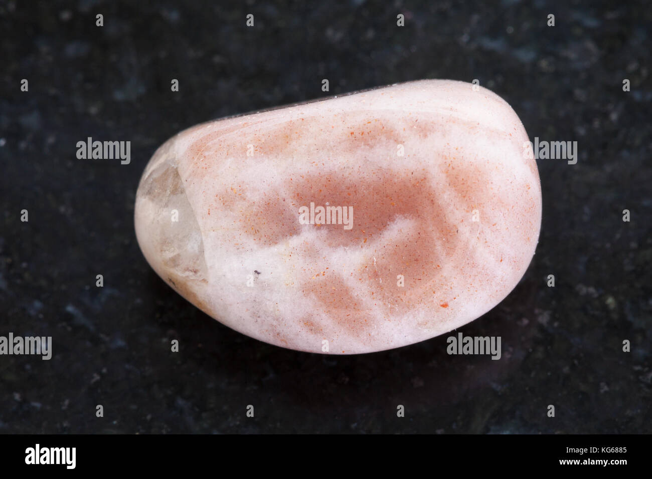 macro shooting of natural mineral rock specimen - tumbled moonstone gemstone on dark granite background Stock Photo