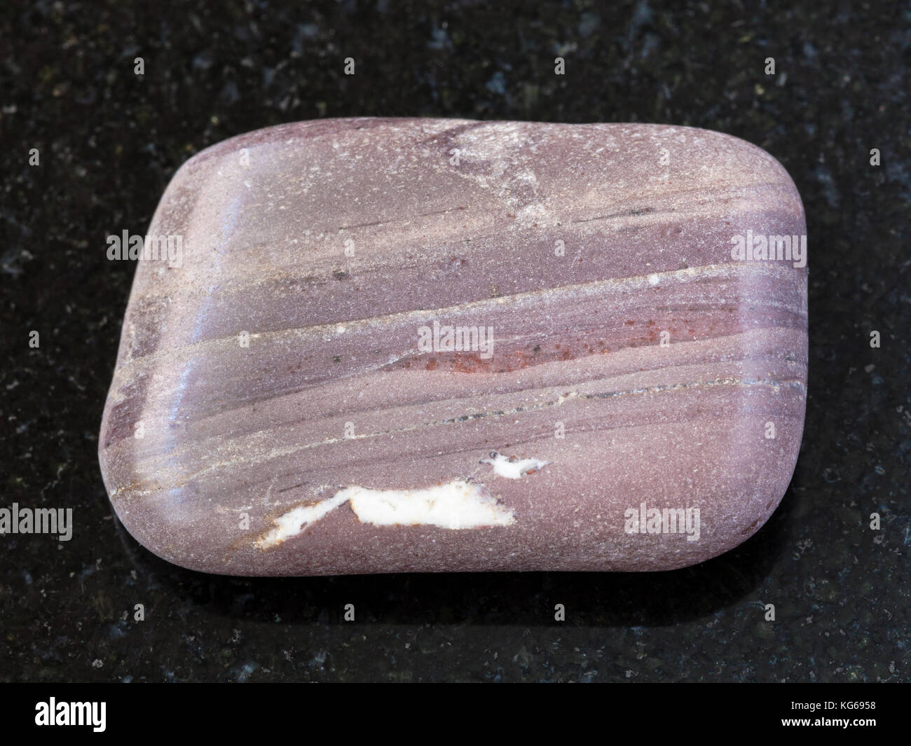 macro shooting of natural mineral rock specimen - polished Argillite gemstone on dark granite background from Sundozero region on Karelia, Russia Stock Photo