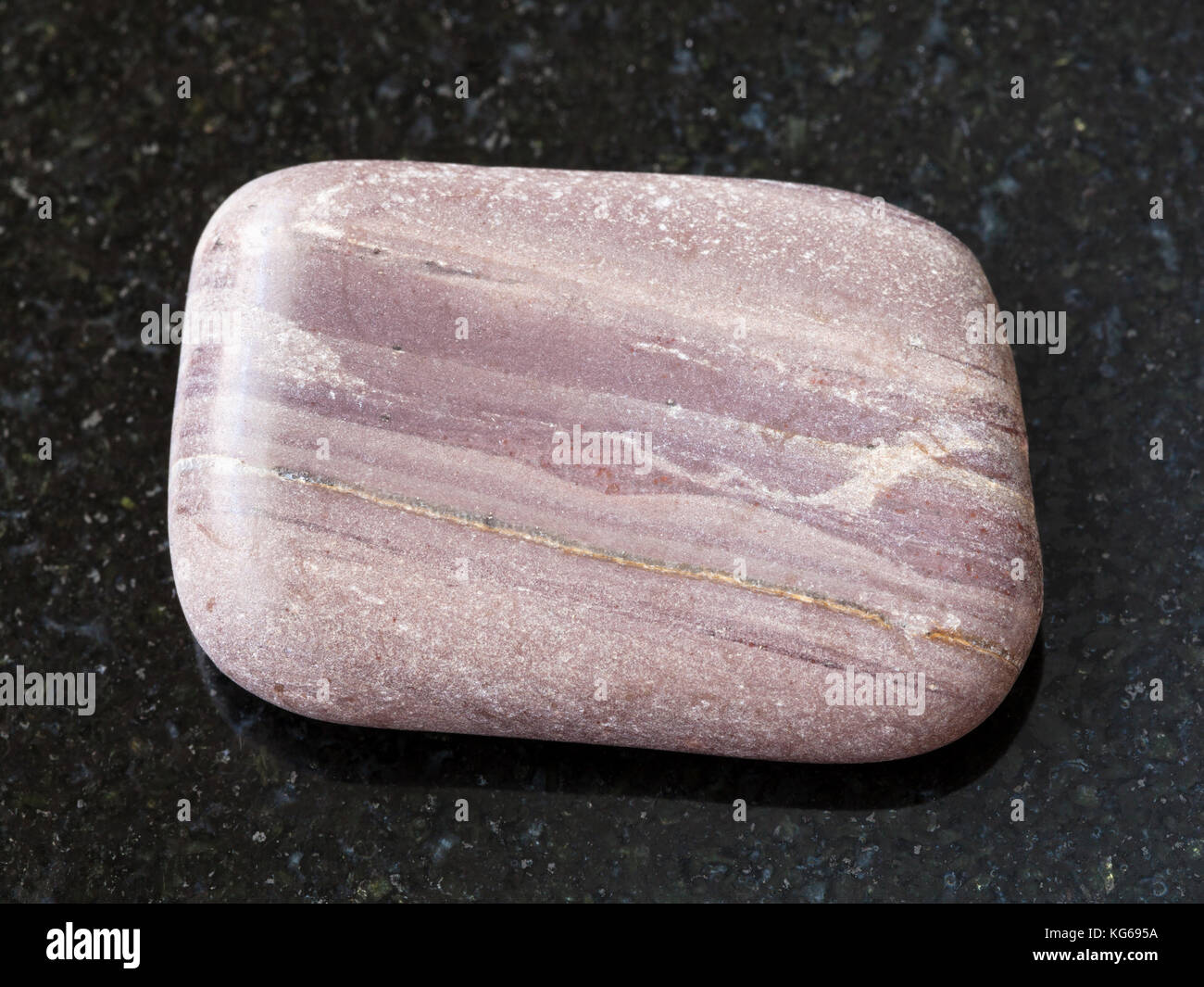 macro shooting of natural mineral rock specimen - tumbled Argillite gemstone on dark granite background from Sundozero region on Karelia, Russia Stock Photo