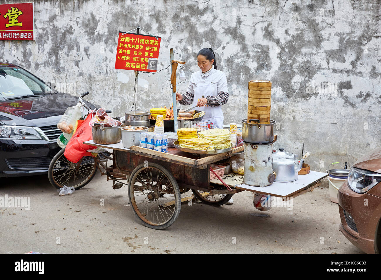 Lijiang, Yunnan, China - September 27, 2017: Woman prepares and sells breakfast food from street stall. Payment via QR code becomes very common in Chi Stock Photo