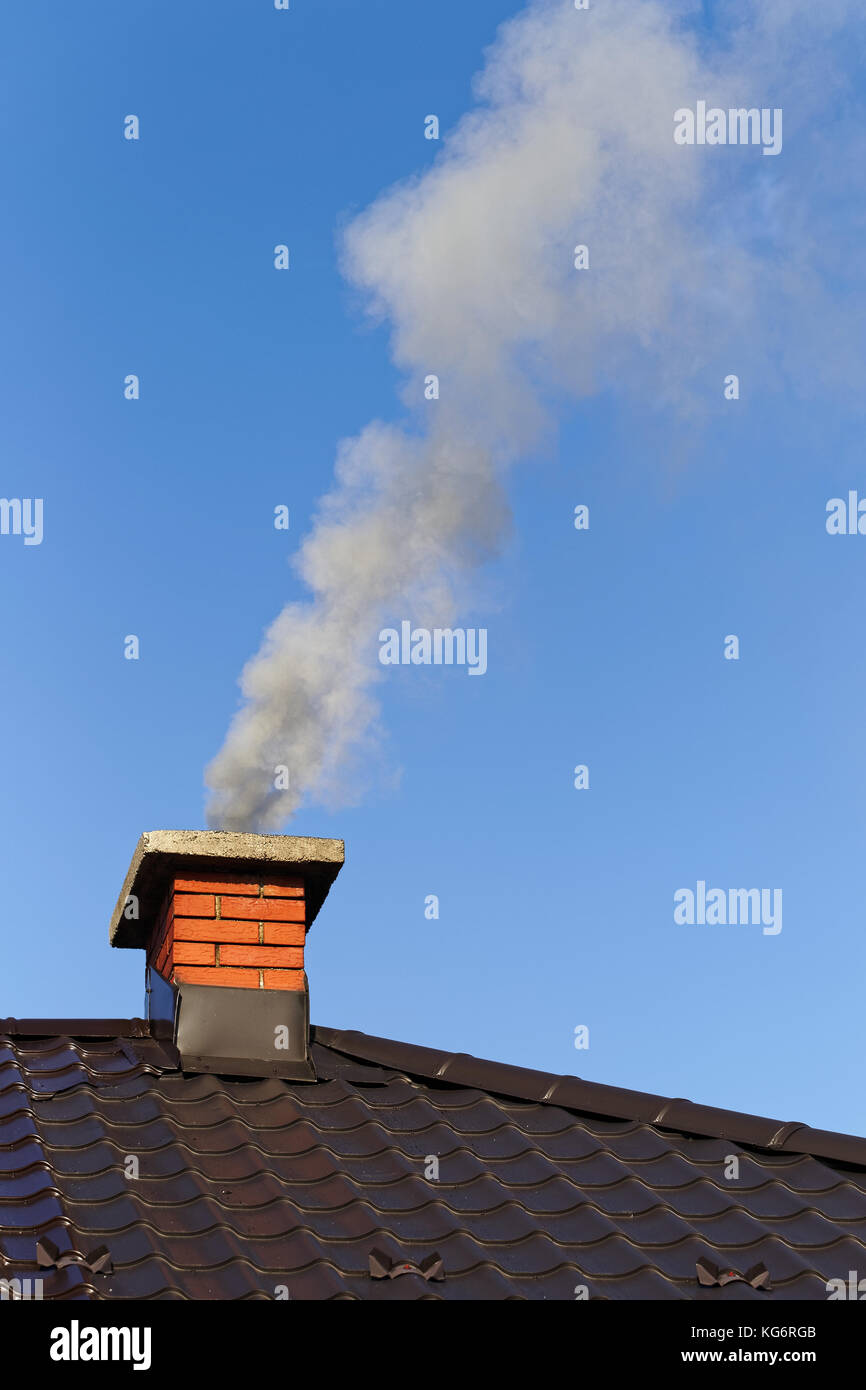 Smoke from brick chimney on the roof against the blue sky Stock Photo