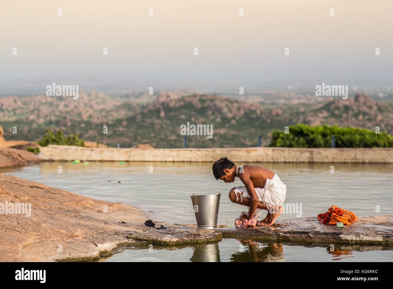 Indian boy washing clothing in front of a impressive view of mountains in south India. Stock Photo