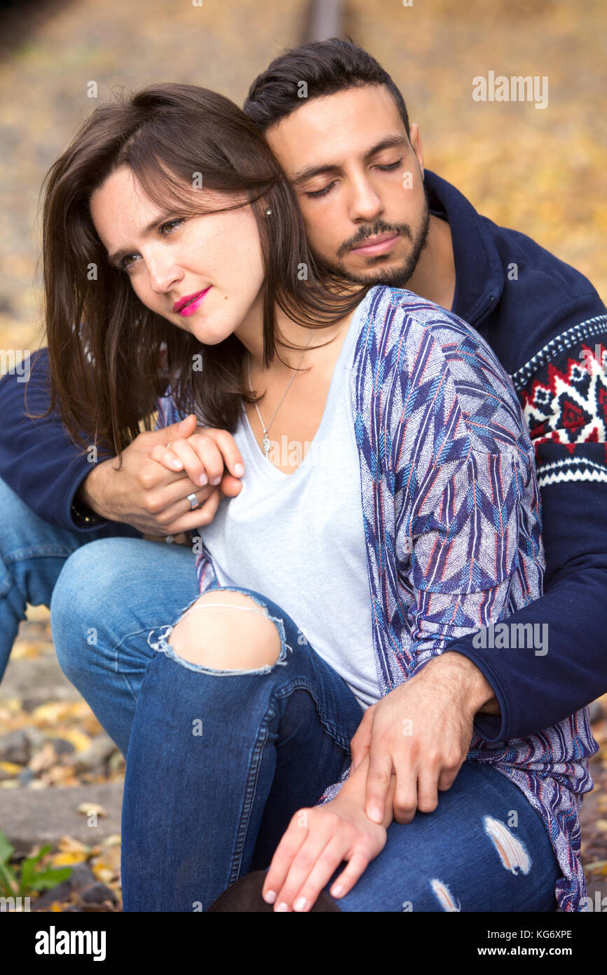 young beautiful couple sitting outside on train tracks and hugging each other Stock Photo