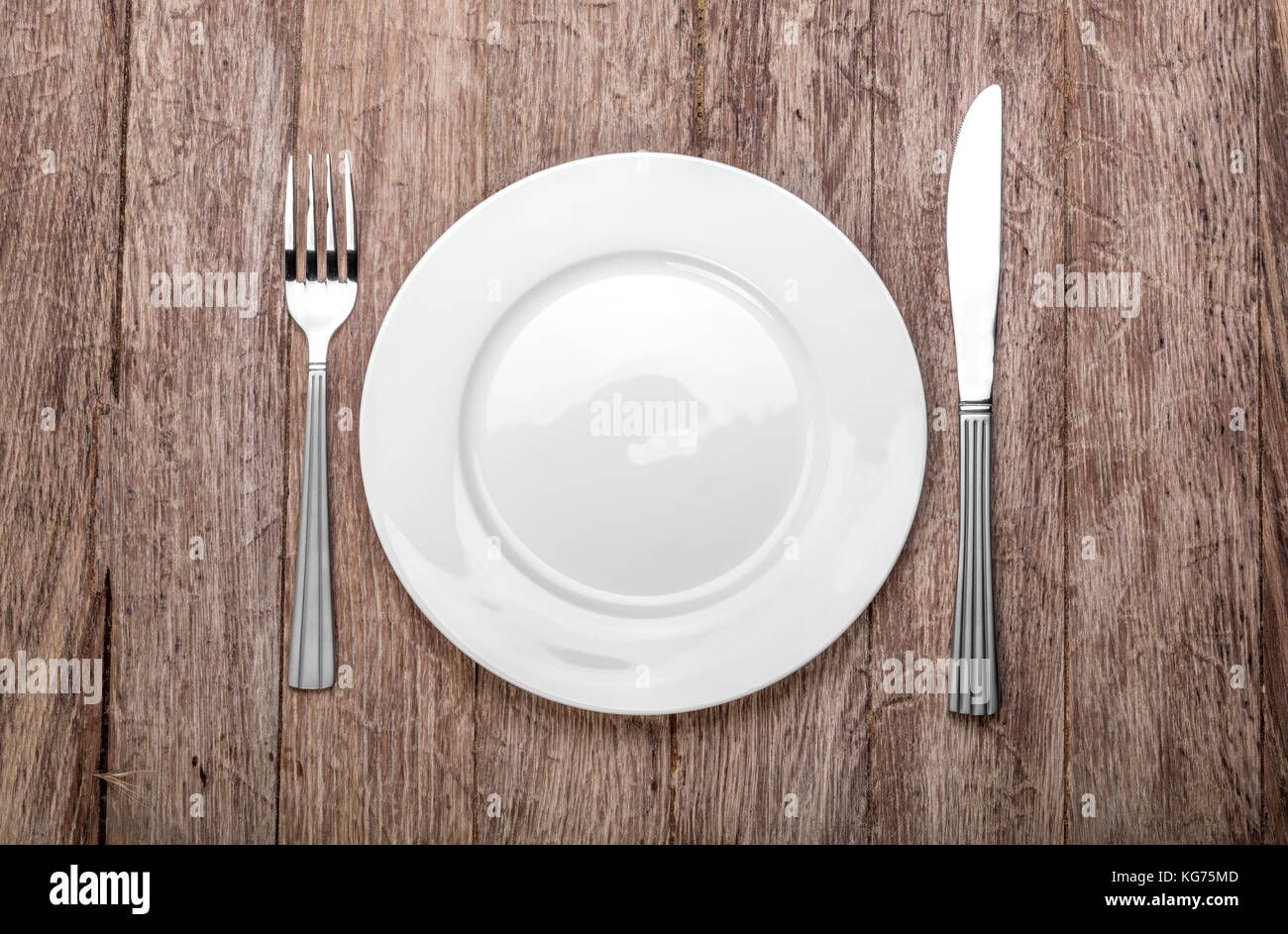Photo of an empty white plate with knife and fork on a rustic wooden ...