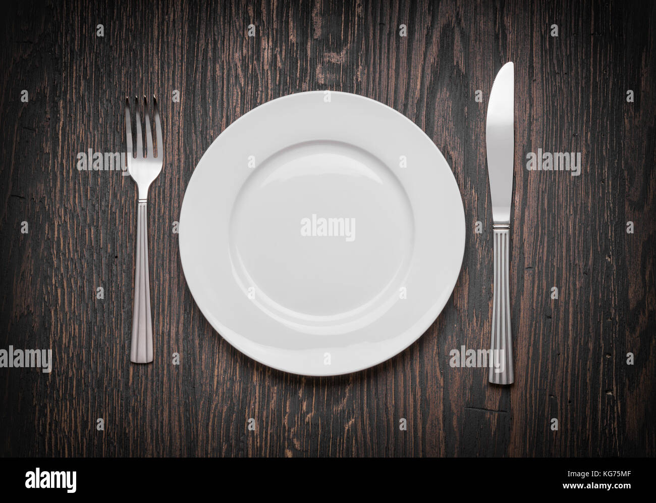 Photo of an empty white plate with knife and fork on a rustic wooden