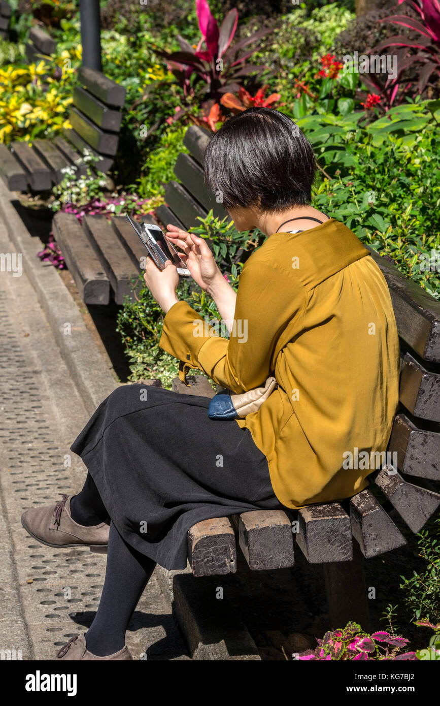 Woman using smart phone in Hong Kong Park, Central, Hong Kong Stock Photo