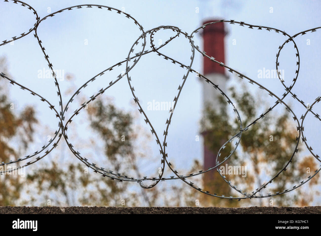 A pipe with smoke behind a fence with barbed wire. Stock Photo