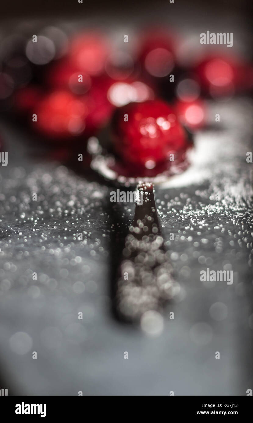 Mixed wild Berries sat on a grey slate serving platter sprinkled in sugar with a shiny spoon Stock Photo