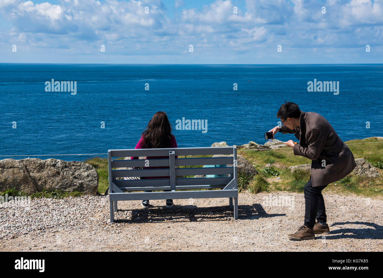 Lands' End, England - April 27, 2017: Tourists sitting on bench at Last/first house at Lands' End in summer taking pictures with phone. Stock Photo