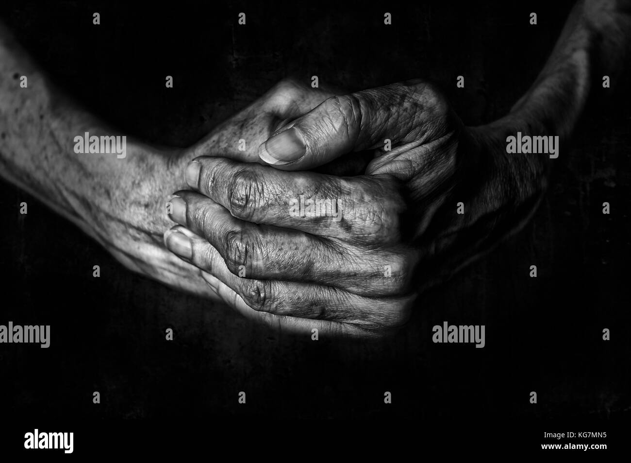 Black and White photo of senior woman hands praying on a dark background texture Stock Photo