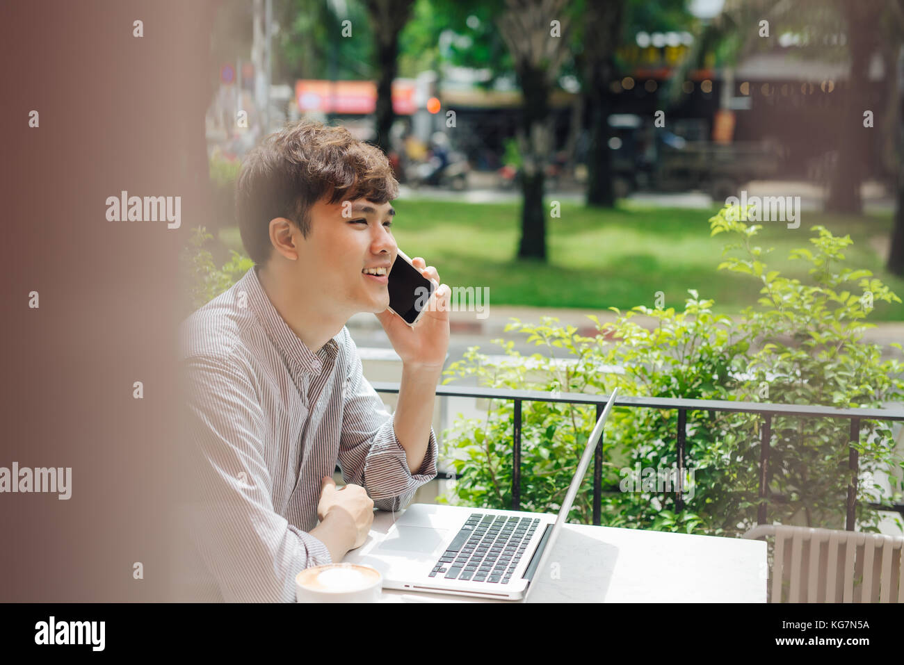 Cheerful young man in casual wear talking on the mobile phone while sitting in cafe. Stock Photo