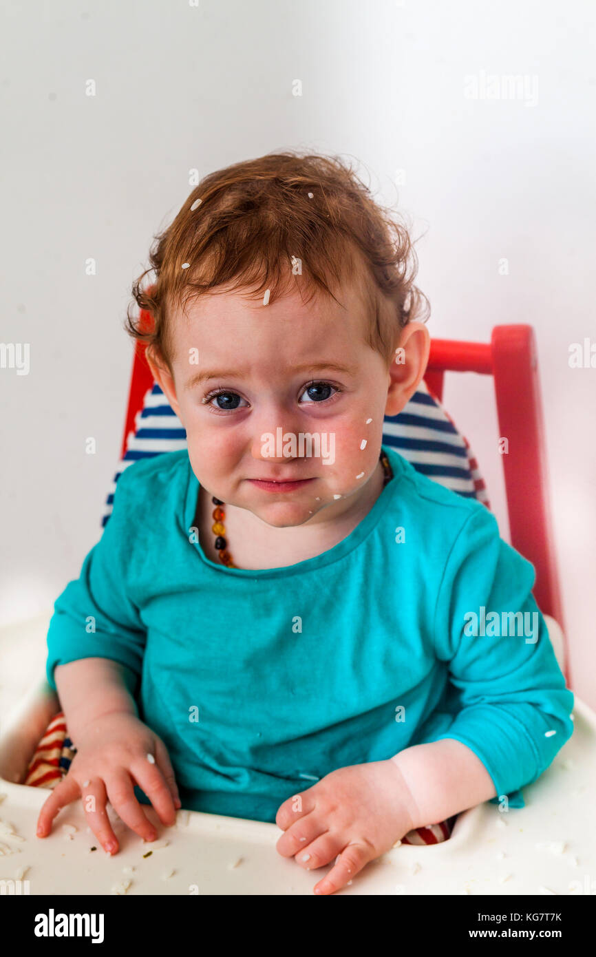 Confused baby making funny offended face in the high chair with rice all over the head - development concept Stock Photo