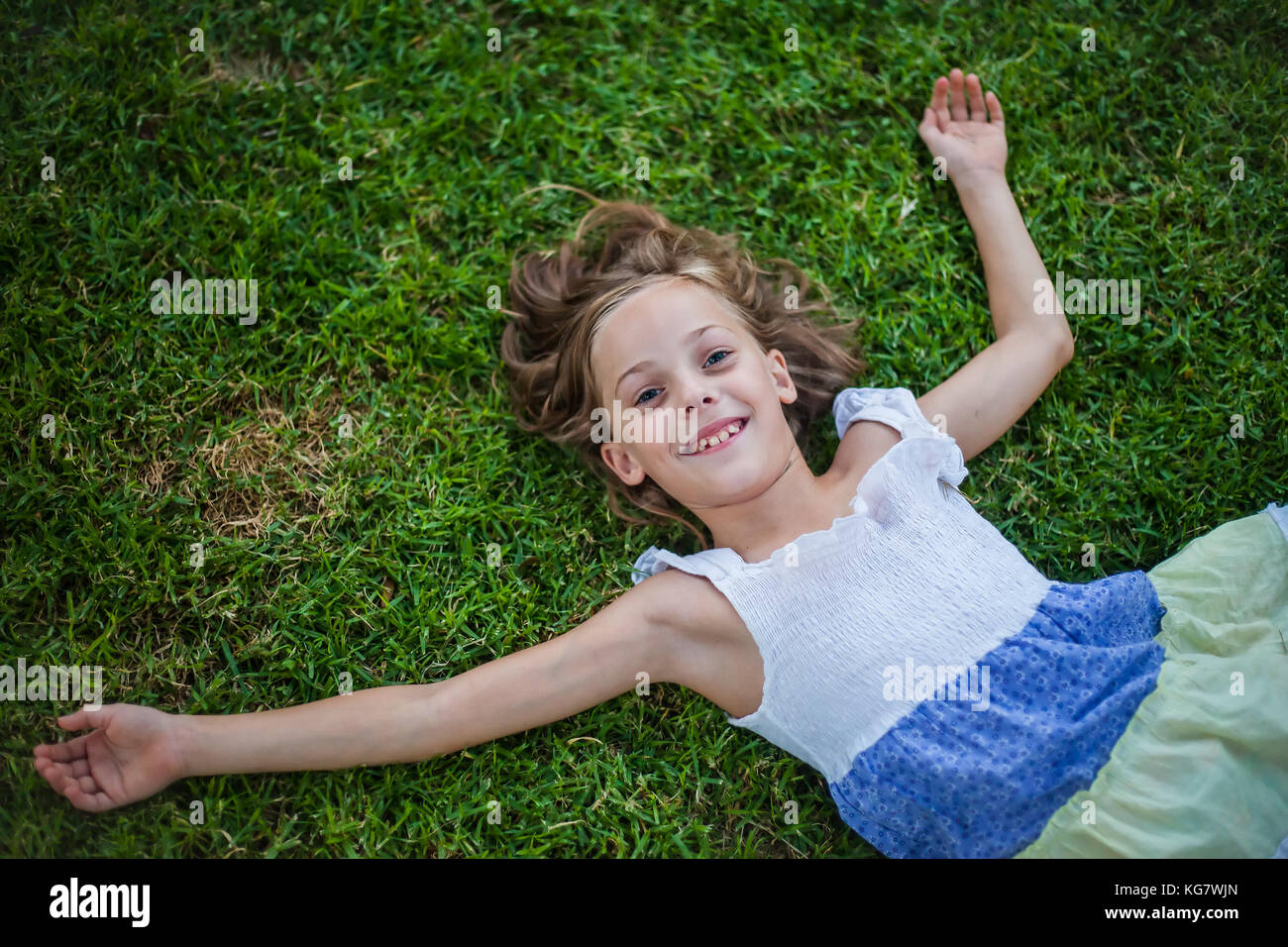 Smiling little girl lying on the grass with happy carefree expression - concept of freedom in childhood Stock Photo