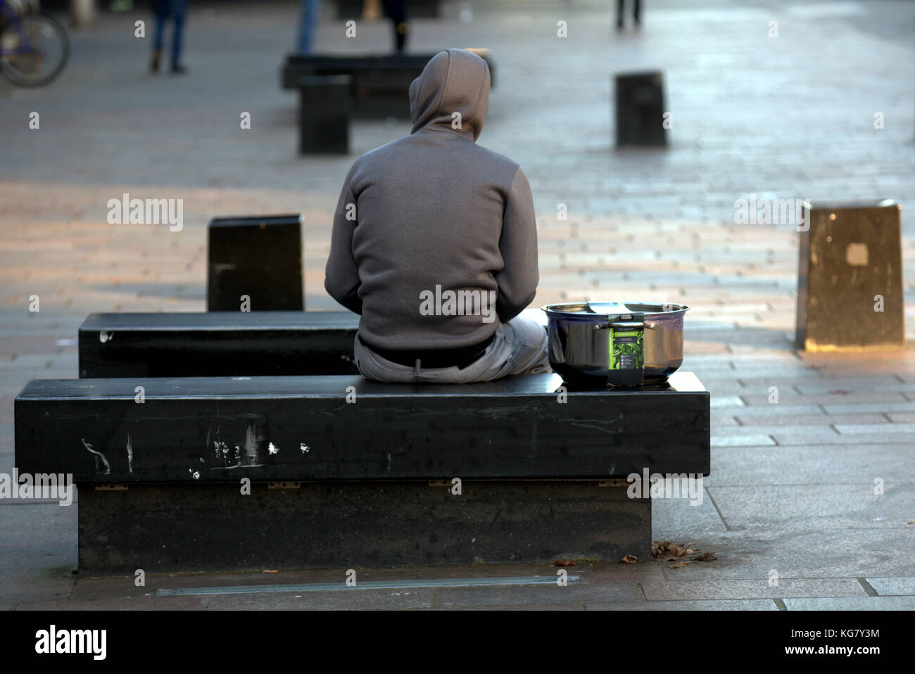 refugee immigrant hoody with a newly bought cooking pot sitting on a  street seat bench viewed from behind Sauchiehall Street, Glasgow, Glasgow City, Stock Photo