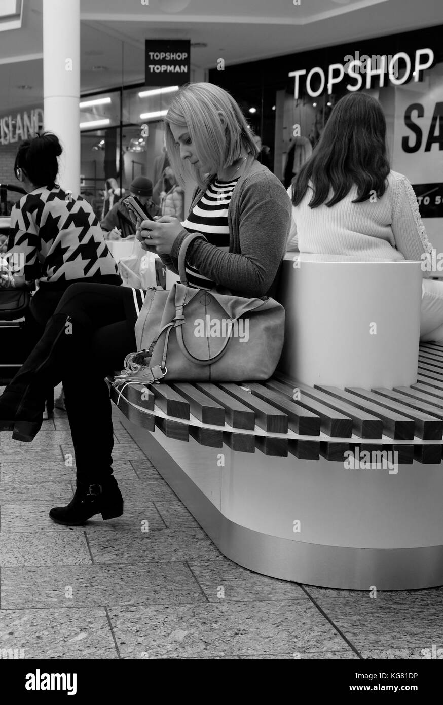 October 2017 - Young woman resting looking at her smart phone on a seat in the middle of Cribbs Causeway shopping mall centre in Bristol, South West. Stock Photo