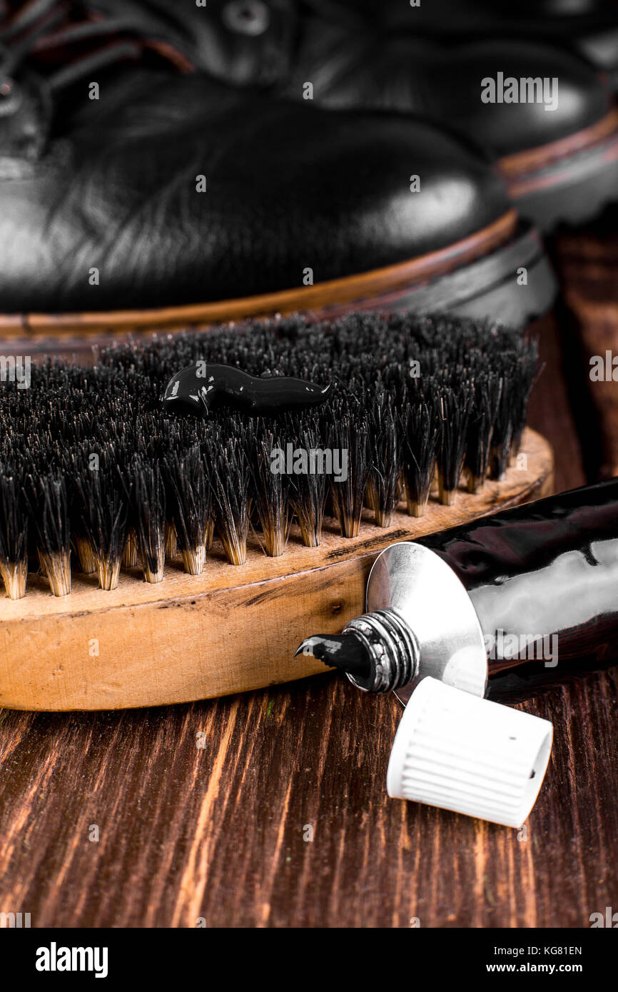 Black boots on wooden background with polishing equipment, brush and