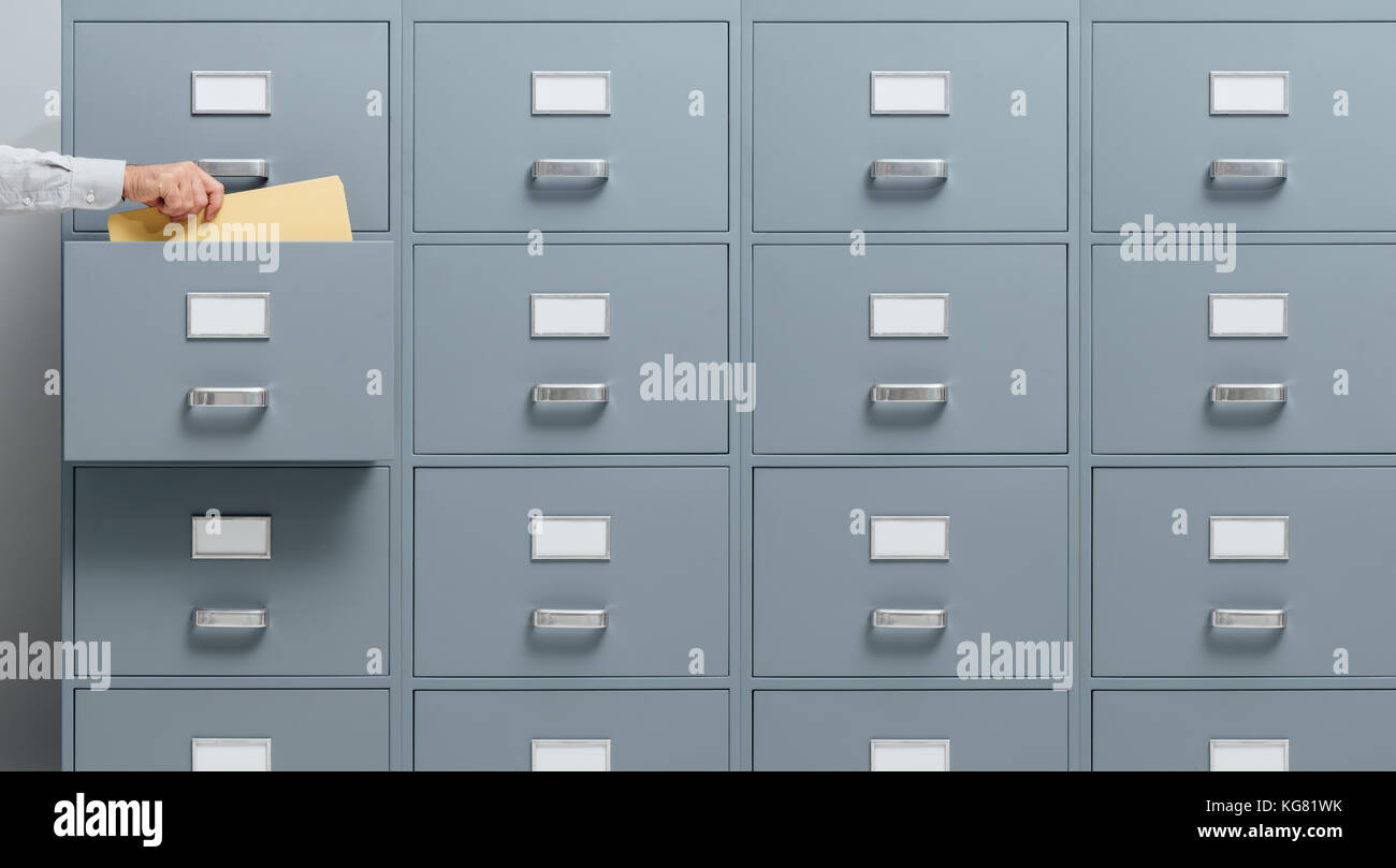 Office worker taking a file from a filing drawer, business and