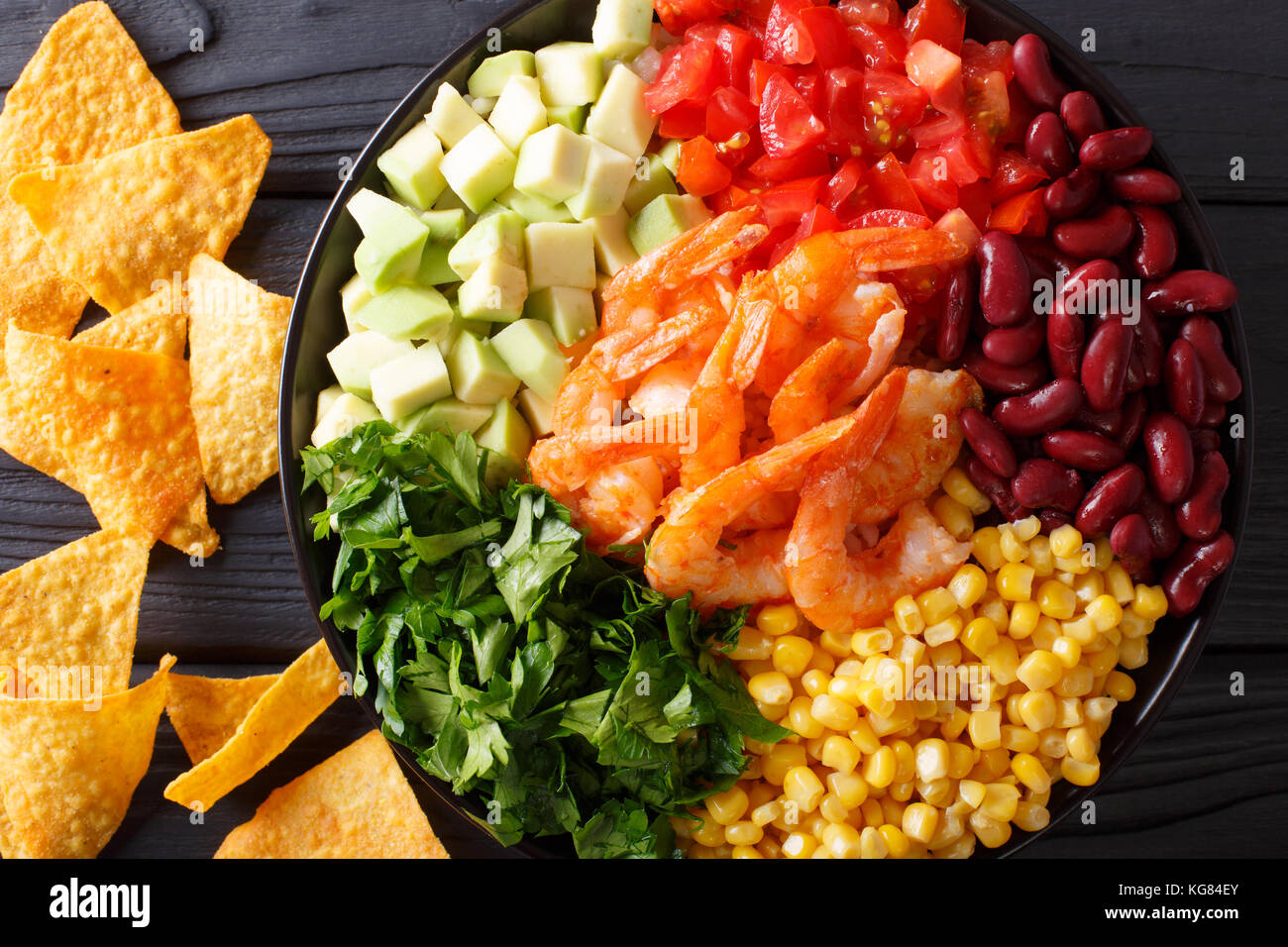 Mexican salad with shrimps, beans, corn, avocado and greens close-up on the table. horizontal top view from above Stock Photo