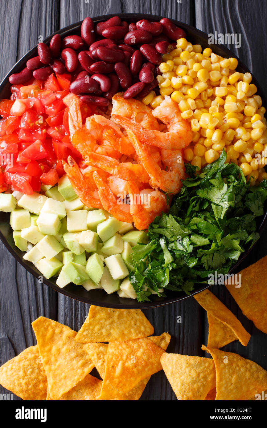 Mexican salad with shrimps, beans, corn, avocado and greens close-up on the table. Vertical top view from above Stock Photo