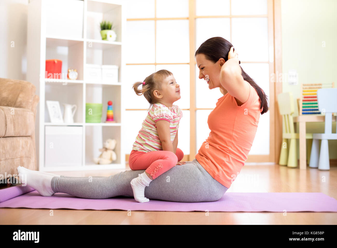Mother and child daughter are engaged in fitness, yoga, exercise at home. Kid and woman swing press on stomach. Stock Photo