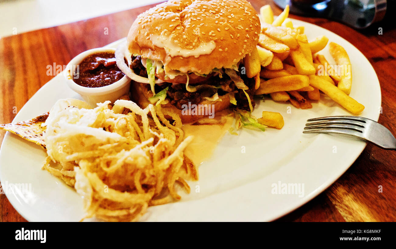 Unhealthy meal with mexican nacho chips, beef burger, loaded with cheese, fries, onion rings and hot souse Stock Photo