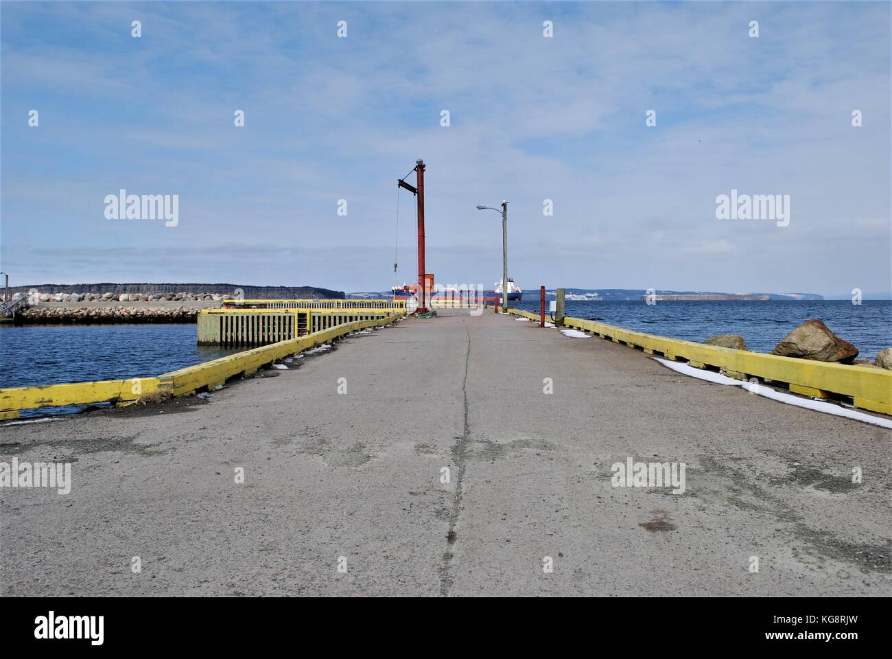 Looking along the length of a pier to where an oil tanker is crossing Conception Bay, Foxtrap, Conception Bay South, Newfoundland Labrador, Canada. Stock Photo