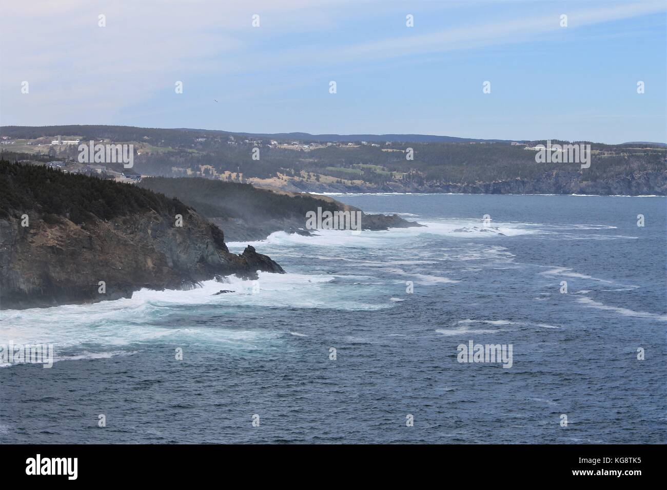 Waves breaking against the cliffs, Logy Bay-Middle Cove-Outer Cove, Newfoundland and Labrador, Canada. Light fog, blue sky and water, white surf. Stock Photo