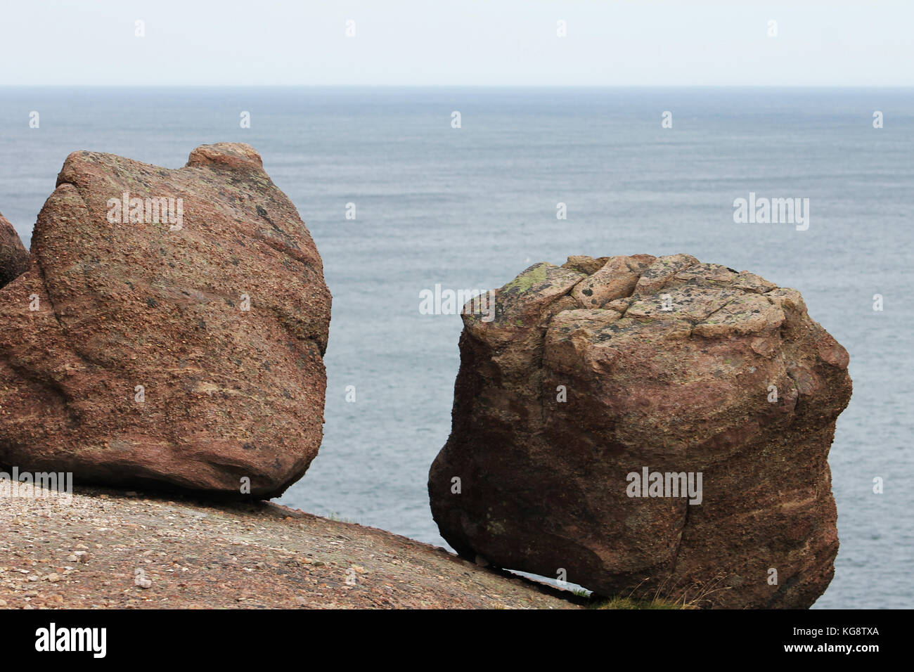 Two large boulders resting on the edge of the cliff, against a background of blue water and blue sky, Signal Hill, Newfoundland.. Stock Photo