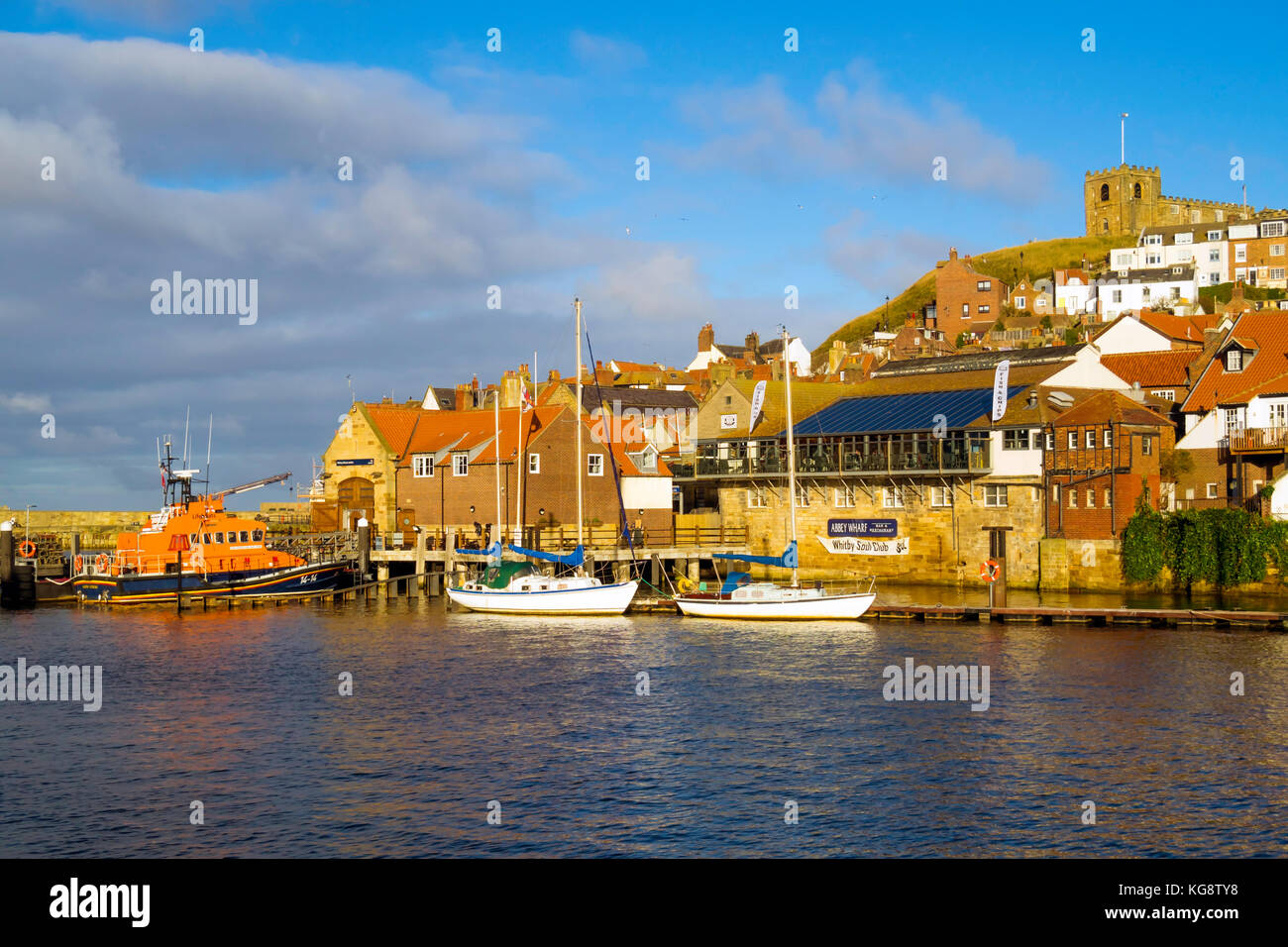 Whitby harbour with the lifeboat station, two moored pleasure sailing boats and St Mary's church in autumn sunlight Stock Photo